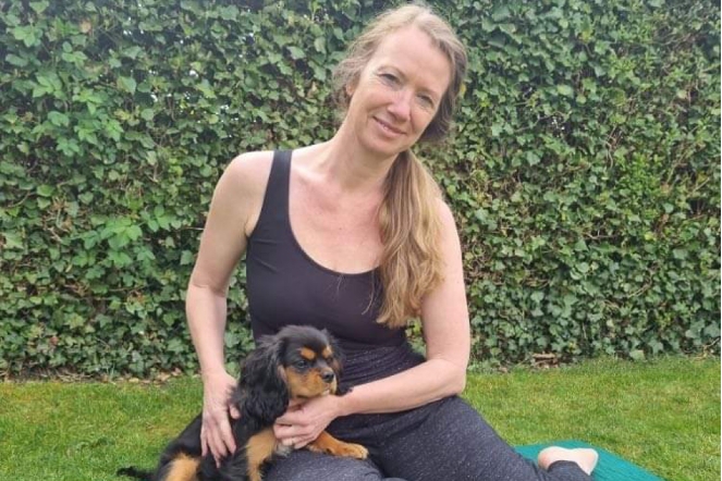 Blonde pilates instructor with long hair sitting on the ground with a black and tan puppy